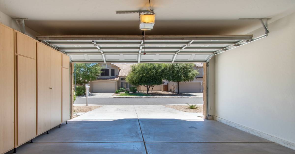 A garage door is completely open. The garage is clean and empty except for a wall of light brown, enclosed storage cabinets.