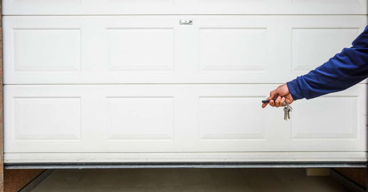 A person pointing a garage door opener remote at a white garage door. The door is only slightly open.