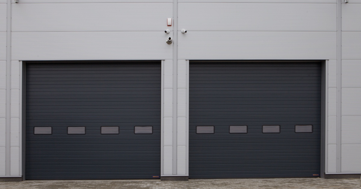 Two dark gray roll up garage doors with windows are completely closed. Three security cameras are mounted above the doors.